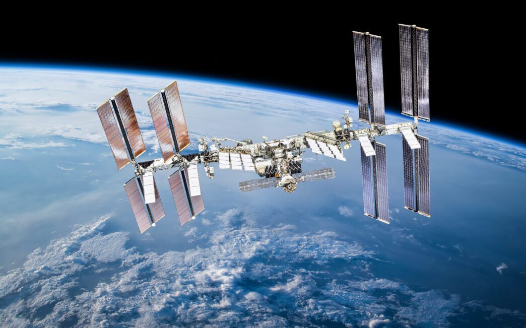 The International Space Station (ISS) orbiting above Earth, with solar panels extended against a dark sky.