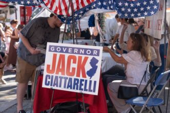 A political campaign sign for "Governor Jack Ciattarelli" displayed at a booth covered by an American flag canopy at a New Jersey festival.