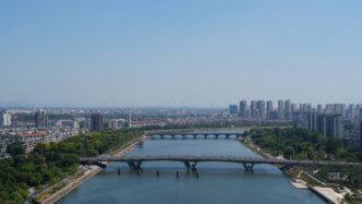 Aerial view of Jinhua city with a wide river, multiple arch bridges, and high-rise buildings.