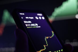 Smartphone screen displaying the Bitcoin price at $121,992.70 and a candlestick chart showing a sharp rise in value.