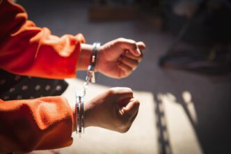 Close-up of a person's hands tightly bound by metal handcuffs, wearing a bright orange shirt.