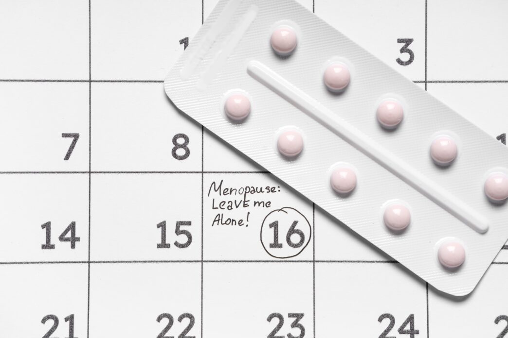 A blister pack of pink pills resting on a calendar with "Menopause: Leave me Alone!" written on day 15.
