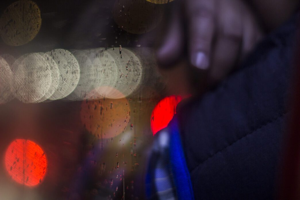 Blurred multi-colored lights and rain streaks seen through glass, suggesting an emergency scene.