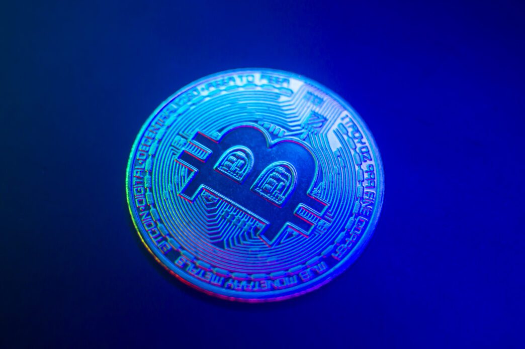 Close-up of a physical Bitcoin coin dramatically illuminated with bright blue and magenta neon lights.
