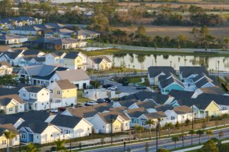 Aerial view of a newly developed suburban housing community with colorful, uniform homes and a pond.