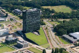 Aerial view of the tall, dark Nexperia headquarters building with a massive green sloped roof structure at Novio Tech Campus in Nijmegen, Holland.