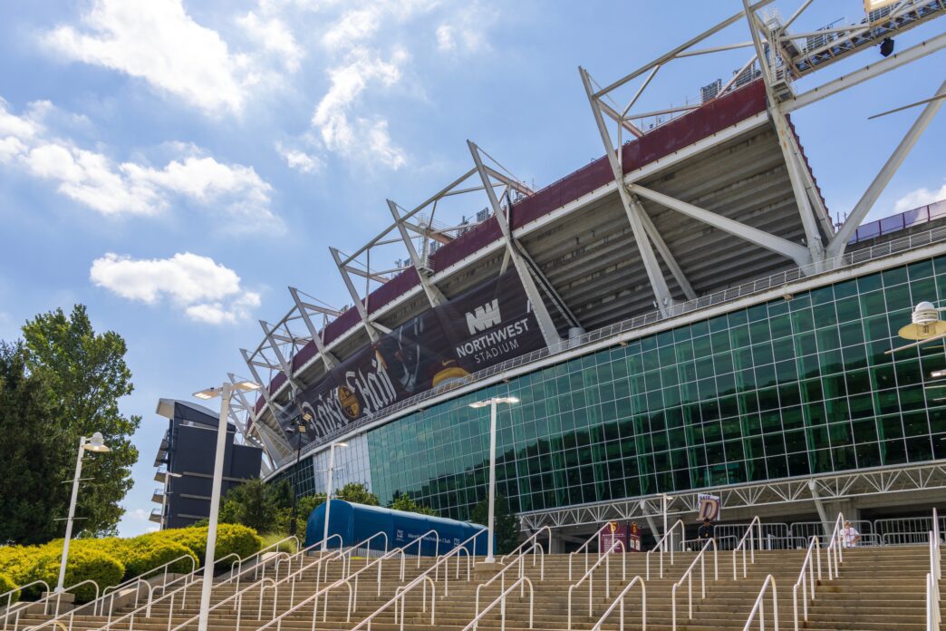 Exterior view of Northwest Stadium, home of the Washington Commanders, with massive structural supports and a glass facade.