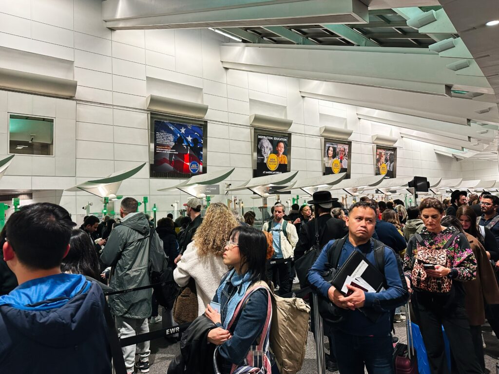 Diverse group of international passengers queuing in a crowded, modern airport customs hall.