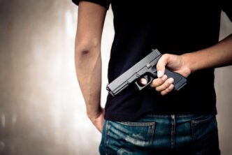 Rear view of a person secretly holding a black handgun behind their back, with their finger on the trigger.