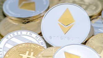 A close-up of a silver physical Ethereum cryptocurrency coin with a gold symbol, surrounded by other crypto tokens.
