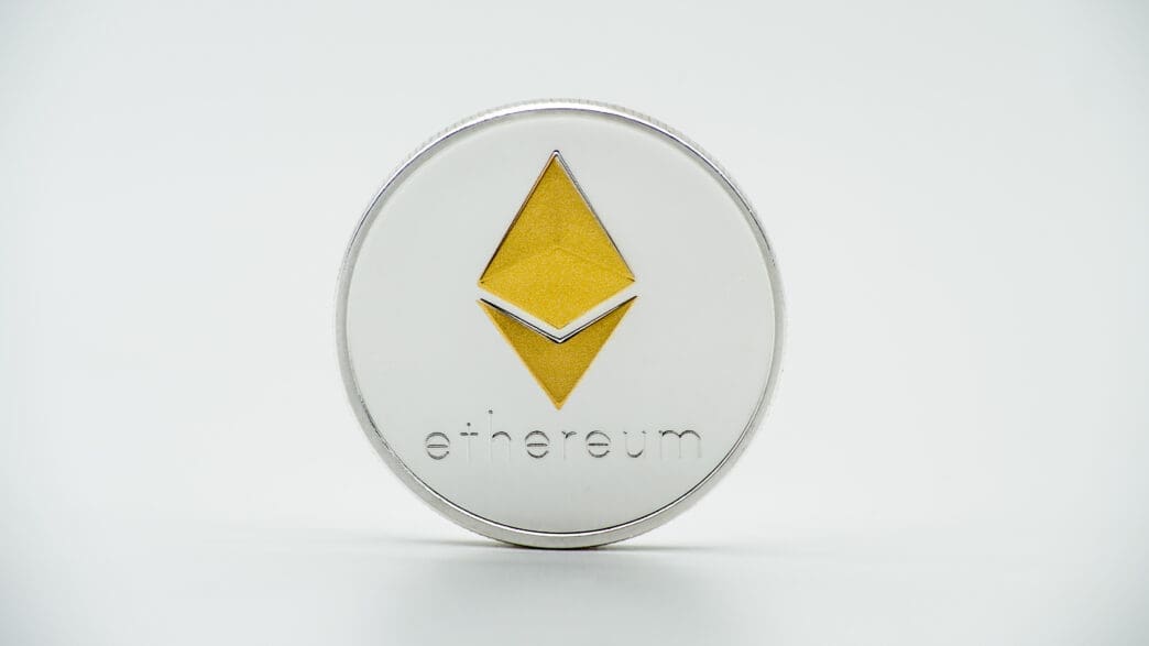 Close-up of a physical silver and gold Ethereum coin with the logo centered on a white background.