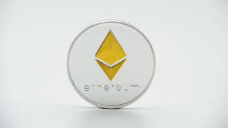 Close-up of a physical silver and gold Ethereum coin with the logo centered on a white background.
