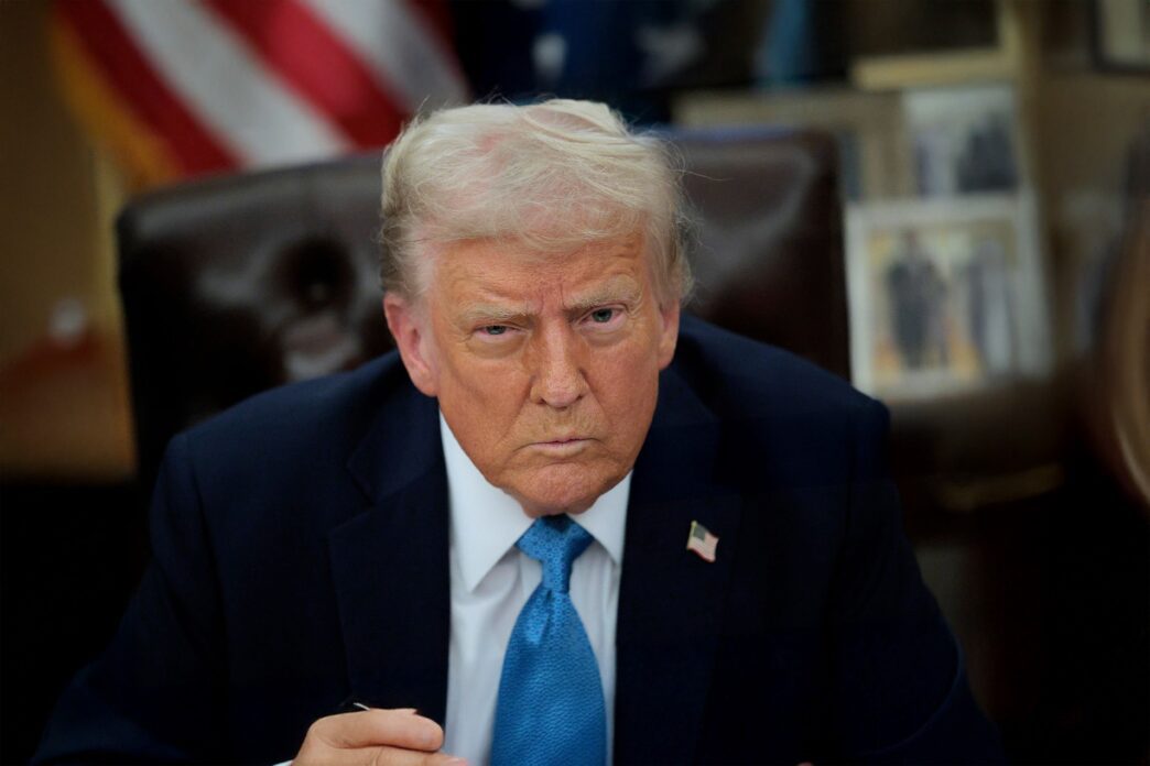 President Trump with a serious expression sitting in the Oval Office to sign an order.
