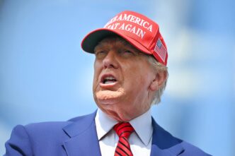 Close-up of U.S. President Donald Trump speaking, wearing a red MAGA hat and blue suit.