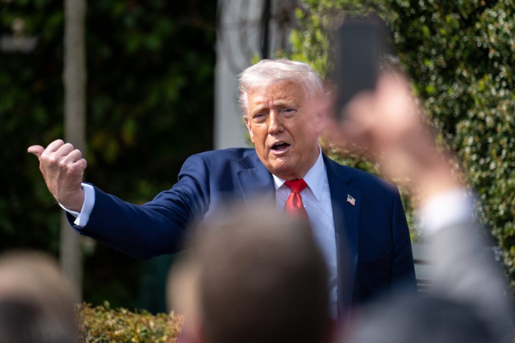 President Donald Trump gesturing with his thumb up while speaking outdoors to a group.
