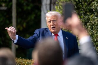 President Donald Trump gesturing with his thumb up while speaking outdoors to a group.
