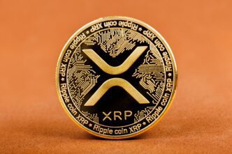 Close-up of a gold and black Ripple XRP cryptocurrency coin on a textured brown surface.