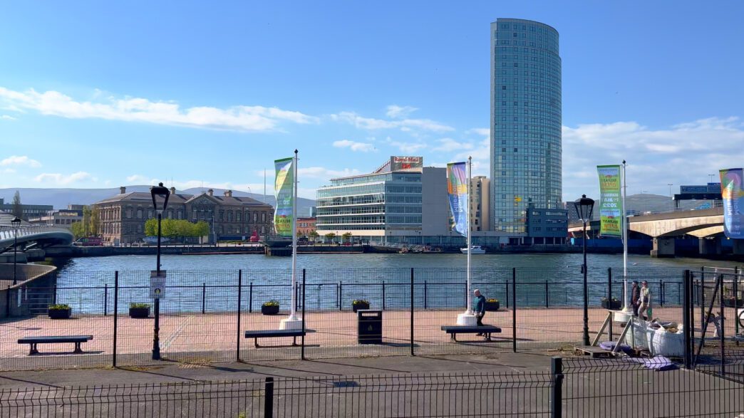 View of the River Lagan in Belfast with a modern skyscraper and historic buildings on the far bank.