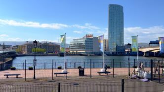 View of the River Lagan in Belfast with a modern skyscraper and historic buildings on the far bank.