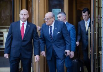 Rudy Giuliani leaving court, flanked by men in suits, after being ordered to surrender valuables.