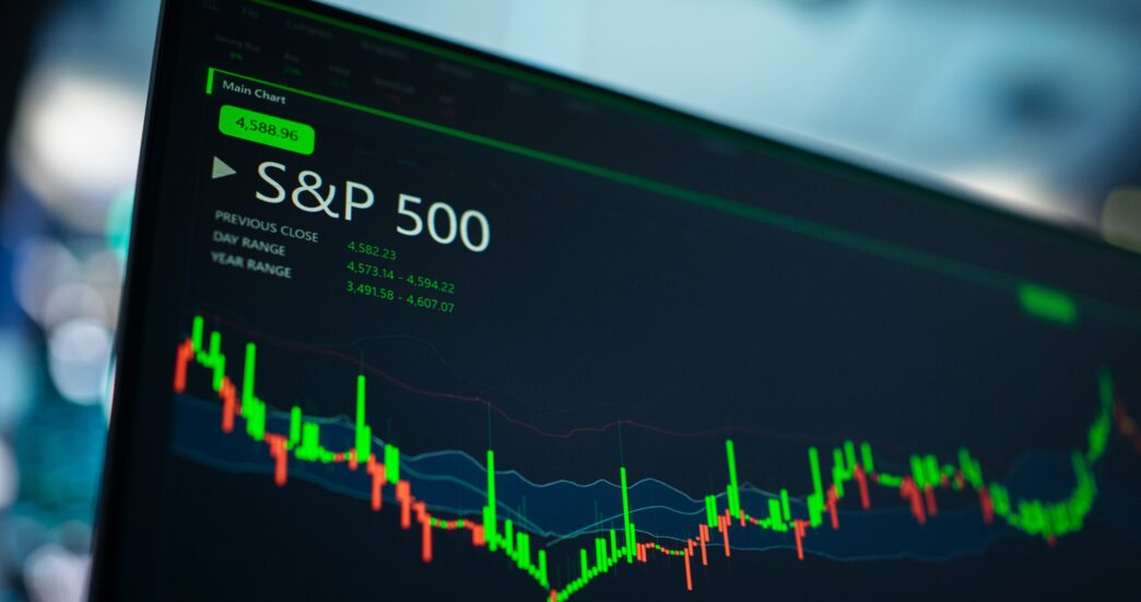 A close-up of a computer screen displaying the S&P 500 index and green/red candlestick charts.