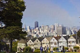 The Painted Ladies Victorian houses are visible from a park foreground, with the San Francisco skyline behind them.