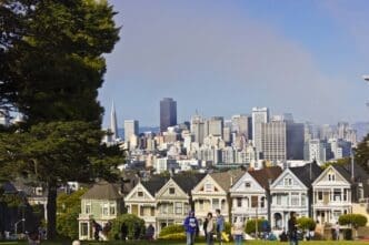 The Painted Ladies Victorian houses are visible from a park foreground, with the San Francisco skyline behind them.