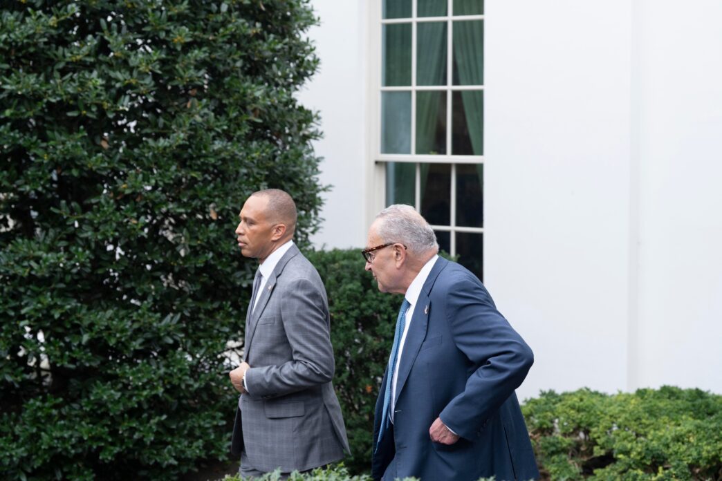 Senate Minority Leader Chuck Schumer and House Minority Leader Hakeem Jeffries walking past a White House building facade and greenery.