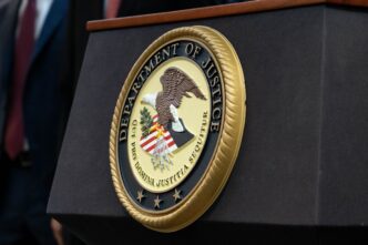 Close-up of the large gold seal of the U.S. Department of Justice displayed on a dark podium.
