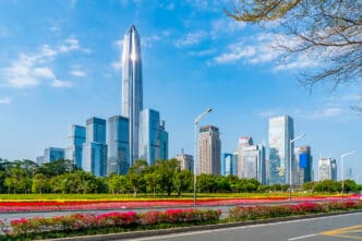 Panoramic view of the tall, modern skyscrapers of the Shenzhen skyline behind a colorful flower garden.