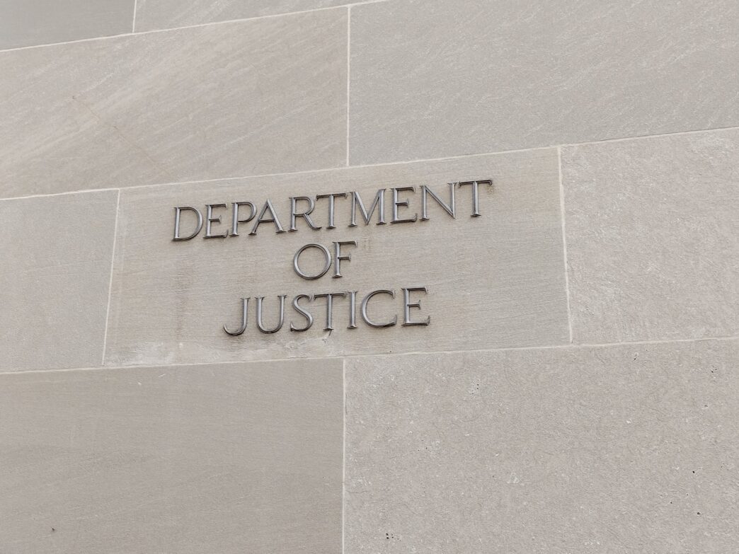 Close-up of the raised metallic letters reading "DEPARTMENT OF JUSTICE" on a stone wall.