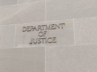 Close-up of the raised metallic letters reading "DEPARTMENT OF JUSTICE" on a stone wall.