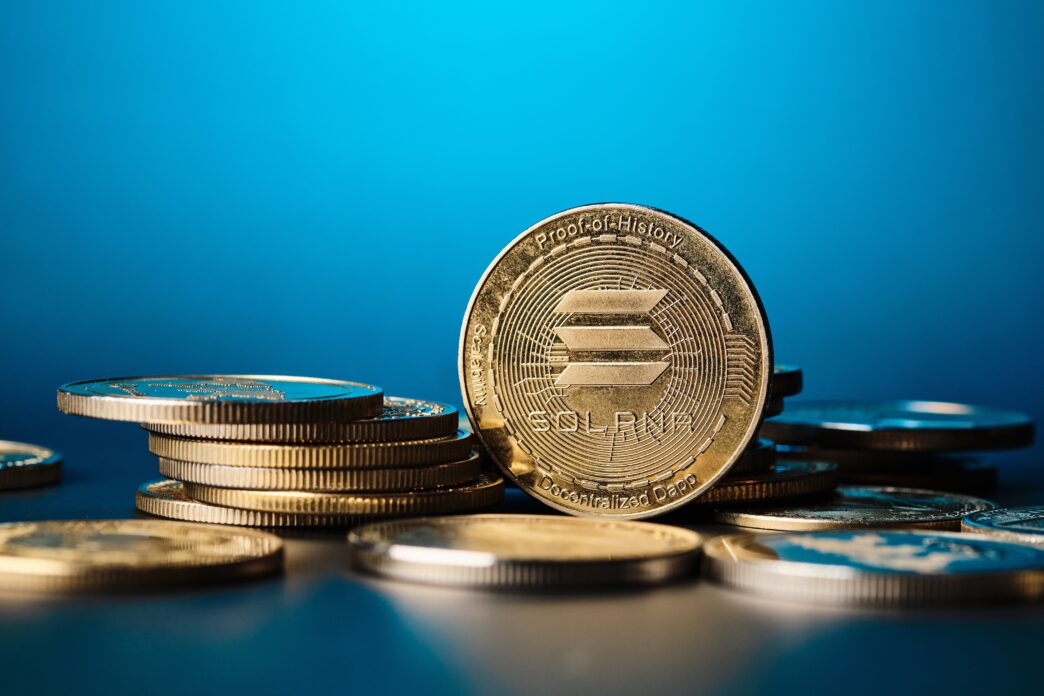 Close-up of a prominent gold Solana coin shining among other coins on a blue background.