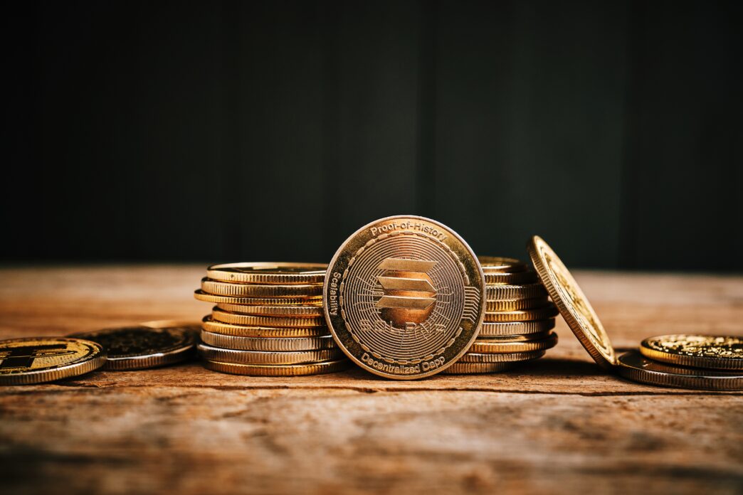 A prominent gold Solana coin leaning against a stack of crypto coins on a rustic wooden table.