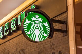 Illuminated, circular Starbucks logo sign mounted on a brick wall, next to neon Chinese characters.