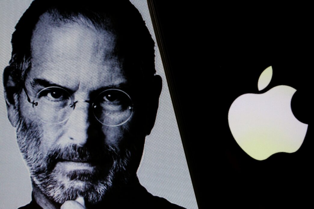 Black and white portrait of Steve Jobs next to the glowing white Apple Inc. logo on a screen.