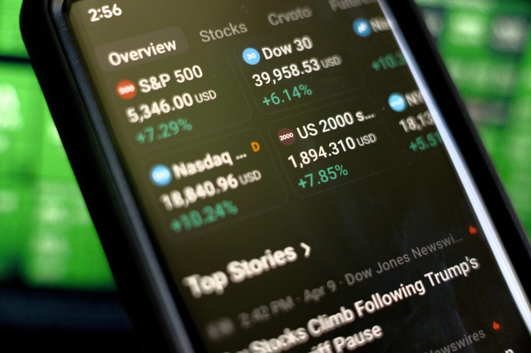 Smartphone screen showing major stock indices (S&P 500, Nasdaq, Dow) all with large green gains.