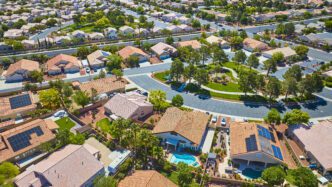 Aerial view of a dense, winding residential neighborhood with terracotta roofs and green parks in a Las Vegas suburb.
