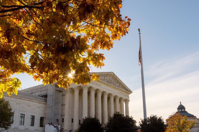 The US Supreme Court building seen through sunlit autumn leaves and an American flag pole.