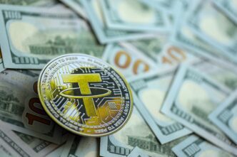 A Tether (USDT) stablecoin rests on a scattered pile of US one hundred dollar bills.