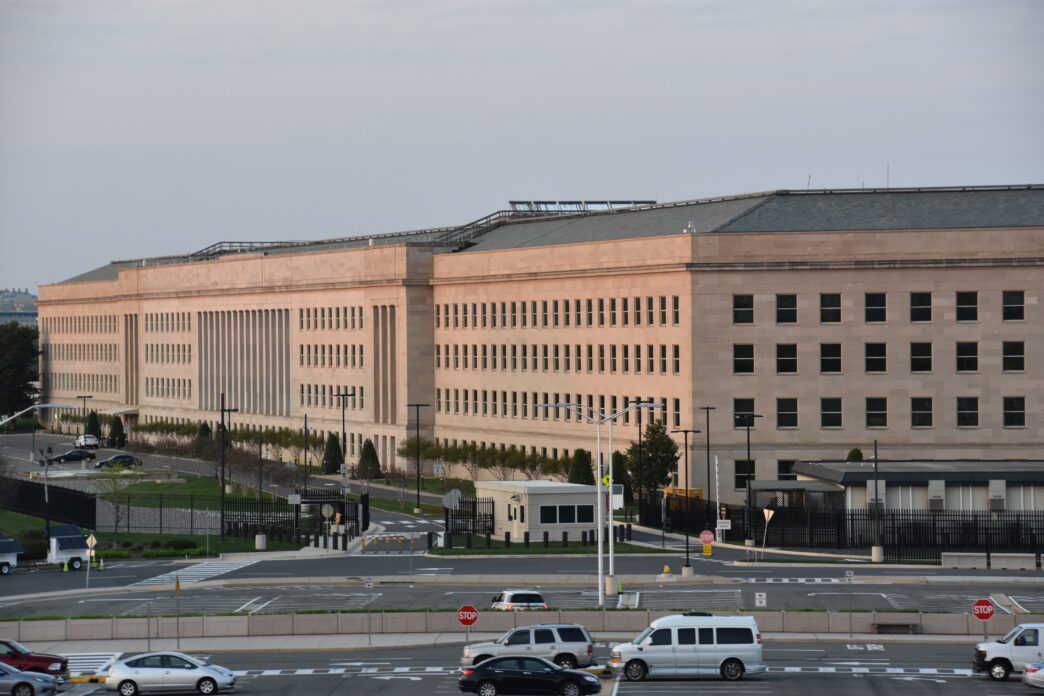 Exterior view of the Pentagon building in Arlington, Virginia, featuring its massive stone facade and many windows, with a parking area in the foreground.