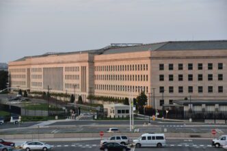 Exterior view of the Pentagon building in Arlington, Virginia, featuring its massive stone facade and many windows, with a parking area in the foreground.