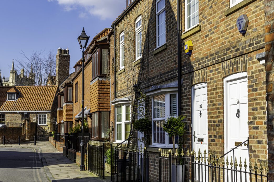 Row of traditional brick terraced houses in a UK suburb on a sunny day.