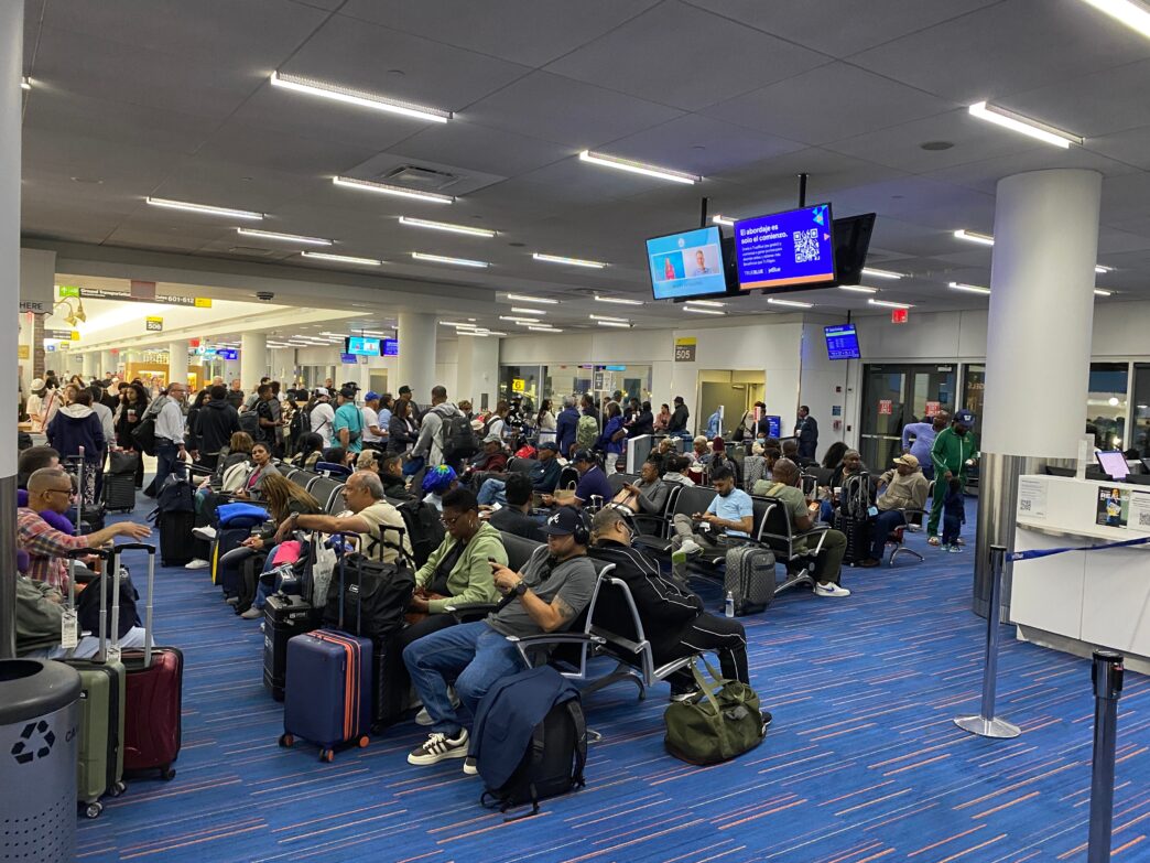 Crowded airport gate area with diverse travelers sitting and waiting for a flight at JFK Terminal 5.