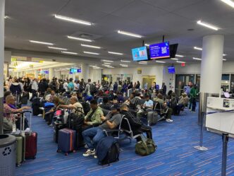 Crowded airport gate area with diverse travelers sitting and waiting for a flight at JFK Terminal 5.