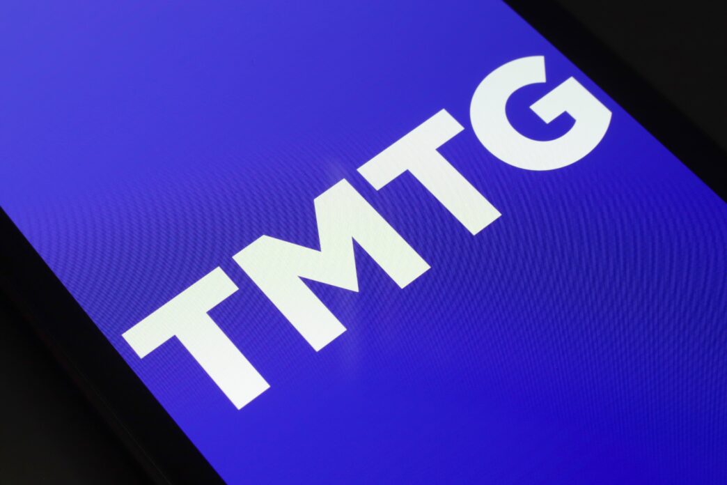 Close-up of the white "TMTG" logo on a vibrant blue background displayed on a smartphone screen.