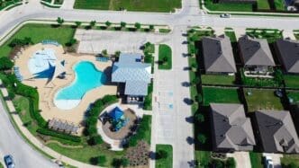 Overhead drone view of a new suburban neighborhood's central amenities, including a swimming pool, clubhouse, and playground.