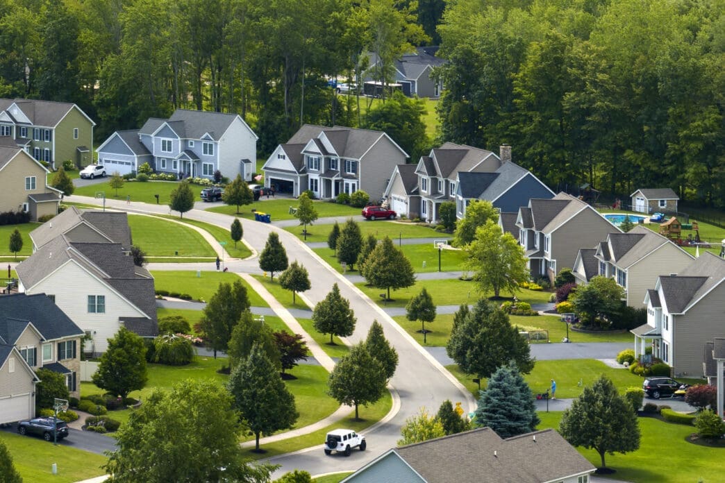 Aerial view of a winding suburban street lined with large, modern houses and mature green trees.