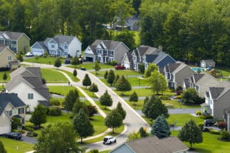 Aerial view of a winding suburban street lined with large, modern houses and mature green trees.
