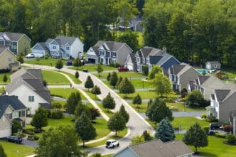 Aerial view of a winding suburban street lined with large, modern houses and mature green trees.